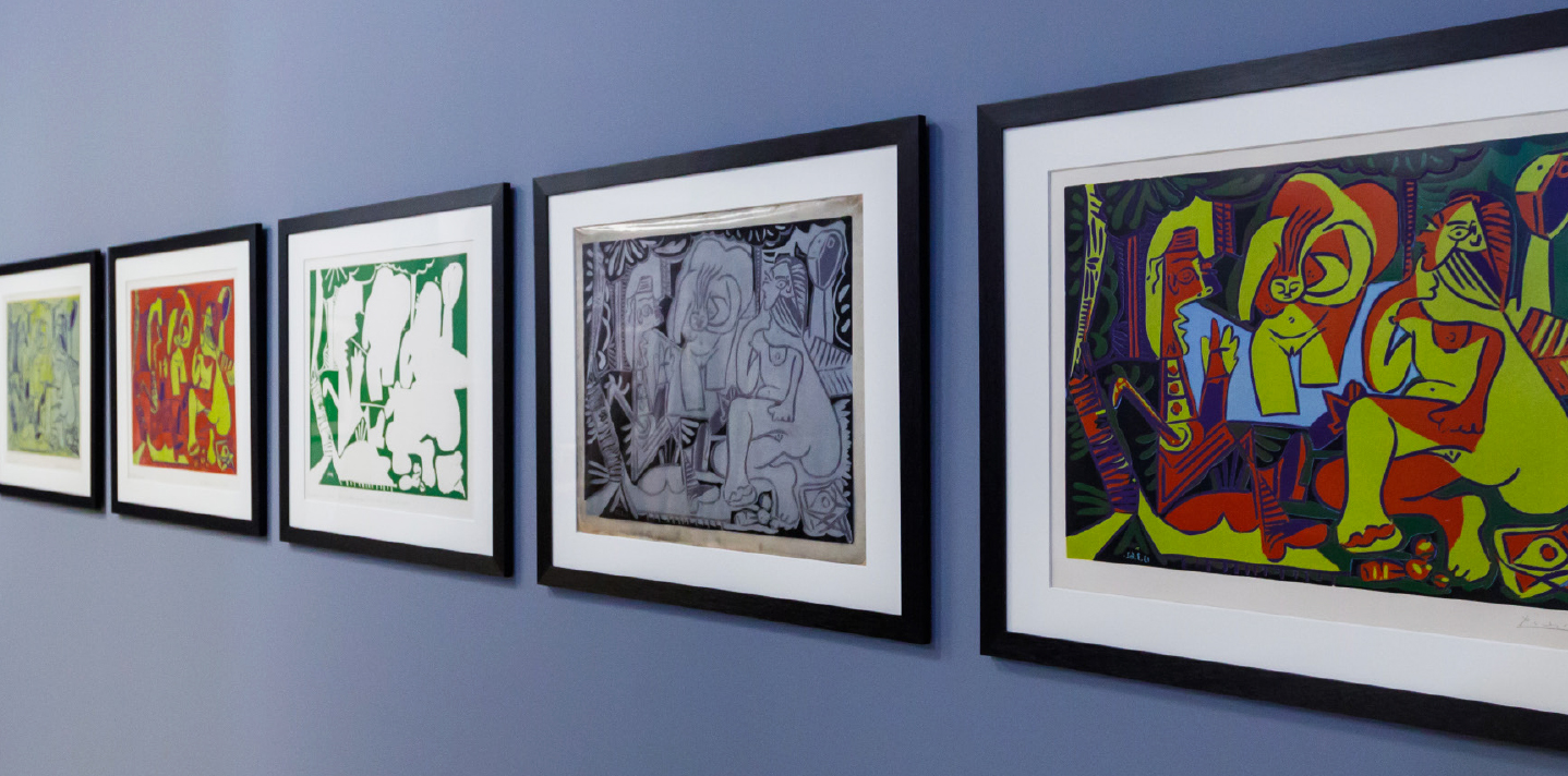 various framed, colorful Picasso works hung up side by side on a blue wall 